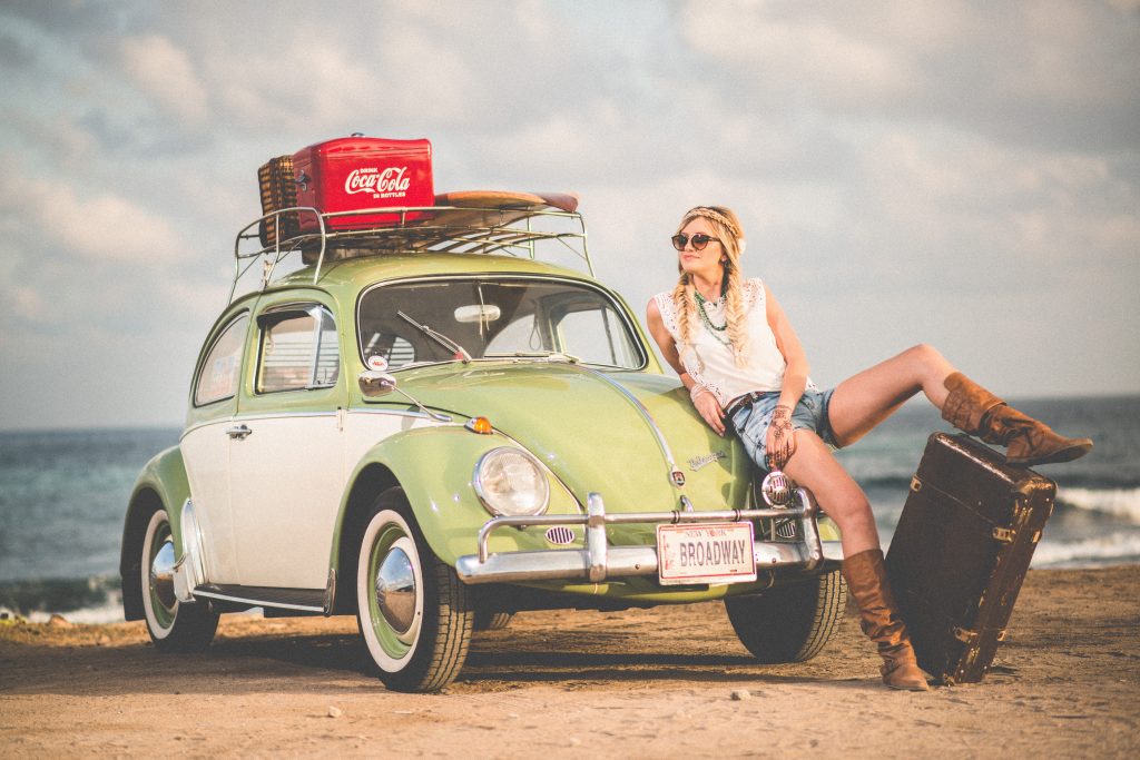 Jeune femme appuyée contre sa voiture verte chargée de bagages pour des vacances